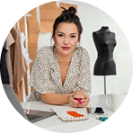 Vrouwelijke modeontwerpster aan het werk aan een bureau met schetsen en gereedschap, bezig met het creatieve kledingontwerpproces in de studio.