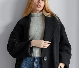 Vrouw in een zwarte jas over een grijze trui, stijlvolle herfstoutfit met een minimalistische mode-uitstraling.