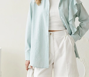 Vrouw in een licht oversized shirt met witte shorts; een strakke, moderne zomeroutfit in zachte, neutrale tinten.